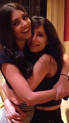 two young women hugging each other in front of a table with pizza on it and one woman smiling at the camera