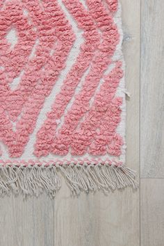 a pink and white rug with fringes on top of wooden floor next to wall