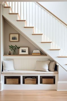 there is a bench under the stairs with baskets underneath it and some pictures on the wall