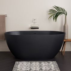 a large black bath tub sitting on top of a bathroom floor next to a rug