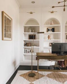 a desk with two computers on it in front of some bookshelves and shelves