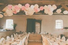 the tables are set with white linens and pink flowers hanging from the rafters