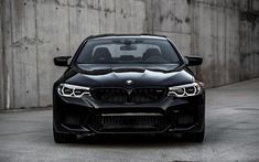 the front end of a black car parked in an empty parking lot with concrete walls behind it