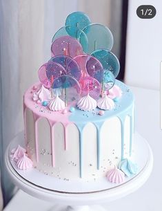 a birthday cake decorated with balloons and confetti on a white table next to a window