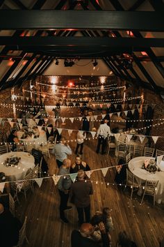 people standing around tables in a room with white tablecloths and lights on the ceiling