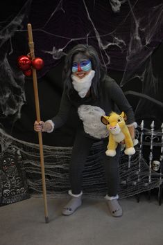 a woman dressed in costume holding a stuffed animal and wearing goggles with a broom