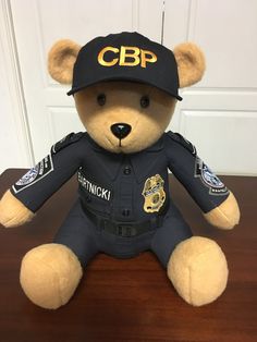 a teddy bear dressed as a police officer sitting on a table with the caption cbp