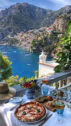 a table with pizza and drinks on it overlooking the water's edge in italy