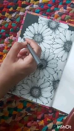 a person is drawing flowers on a piece of paper with a marker and pen in their hand