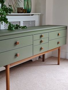 a green dresser with brass handles and drawers in a room next to a white wall