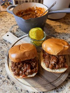 two sloppy joe sandwiches on a cutting board next to a bowl of macaroni and cheese