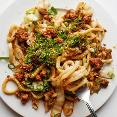 a white plate topped with noodles and meat next to a fork on top of a table