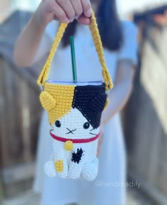 a person holding a small crocheted purse with a cat on it's side