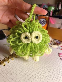 a hand holding a crocheted green monster ornament on top of a table