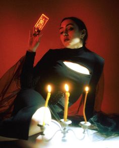 a woman sitting on a table with candles in front of her and holding a card