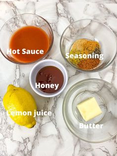 four bowls with different types of sauces in them on a marble counter top next to two lemons