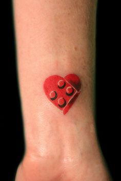 a small red heart shaped tattoo on the wrist with two dices attached to it