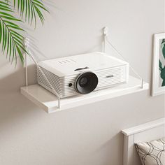 a white projector sitting on top of a shelf next to a potted plant