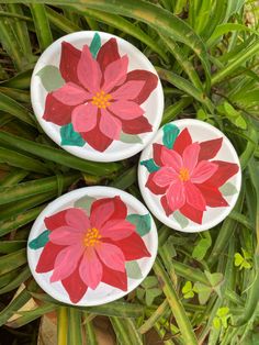 three plates with flowers painted on them are sitting in the grass next to some plants