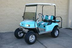 a light blue golf cart parked in front of a building with two seats on it