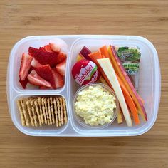 a plastic container filled with fruit, crackers and veggies on top of a wooden table