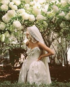 a woman in a wedding dress standing under a tree with white flowers on the branches