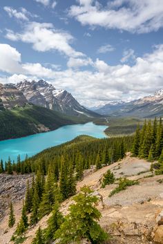 a lake surrounded by trees and mountains under a blue sky with clouds in the background