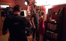 a man and woman standing in front of a book shelf next to a cameraman