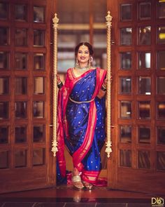 a woman in a blue and red sari is standing on a wooden door way