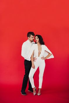 a man and woman standing next to each other in front of a red background wearing white