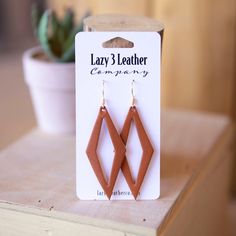 a pair of leather earrings sitting on top of a wooden table next to a potted plant