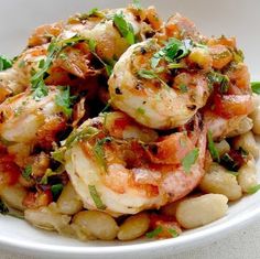 a white bowl filled with shrimp, beans and garnished with parsley on top