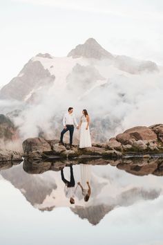 a man and woman standing on top of a mountain next to a lake