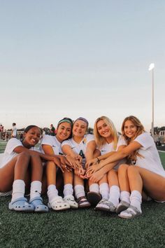 a group of young women sitting on top of a soccer field holding their hands together