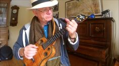 an older man is playing the ukulele guitar in his living room while wearing a hat and scarf