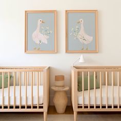 two framed pictures hang on the wall above cribs in a baby's room