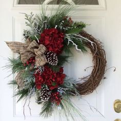 a wreath on the front door with pine cones and red carnations is adorned with greenery