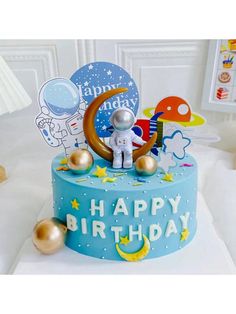 a blue birthday cake with an astronaut on top and gold decorations around the edges, sitting on a white surface