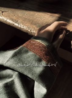 a person's hand resting on top of a wooden table with writing in arabic