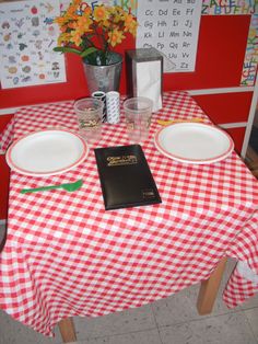 a red and white checkered table cloth with two empty plates on it next to a book