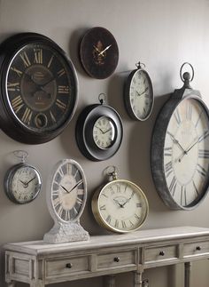 several clocks are hanging on the wall next to a table with an old fashioned console