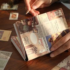 a person is writing on an open book with stamps and paper around the pages that have been cut out