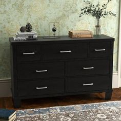 a black dresser sitting in front of a wallpapered wall with flowers and books on top