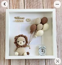 a crocheted lion holding balloons in a white shadow box with the word welcome home on it