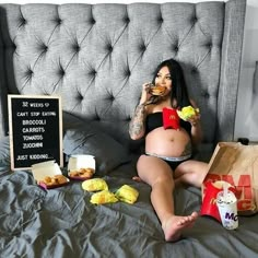 a pregnant woman sitting on a bed eating food and holding a drink in her hand