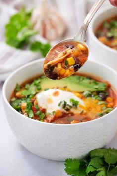 a spoon full of mexican soup with avocado and sour cream