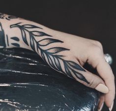 a person's hand with a black and white tattoo on their left arm, resting on a chair