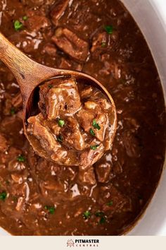 a wooden spoon filled with beef stew on top of a table