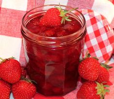 some strawberries are sitting next to a jar of jam on a checkered tablecloth