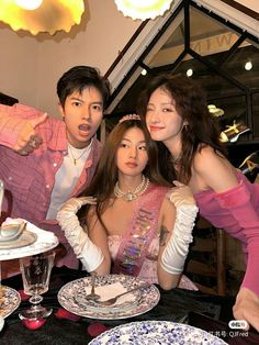 three people standing in front of a table with plates on it and one person pointing at the camera